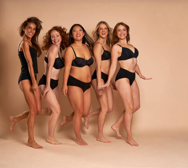 Grupo de mujeres alegres en ropa interior negra de pie y sonriendo hacia la cámara - Foto, Imagen