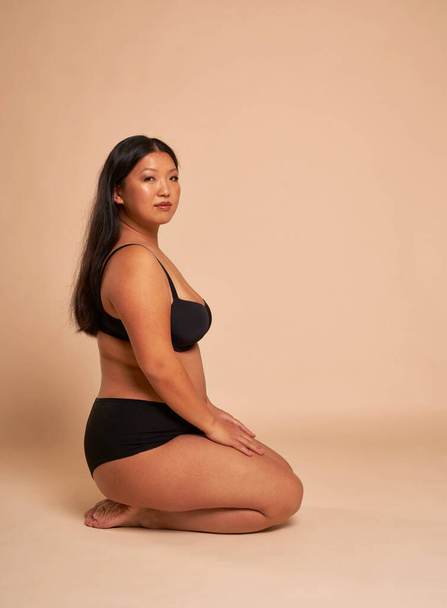 Image verticale de la femme chinoise en sous-vêtements assise sur le sol dans le studio - Photo, image