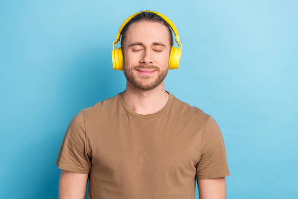 Photo of dreamy positive guy dressed beige t-shirt headphones enjoying music isolated blue color background. - Foto, afbeelding