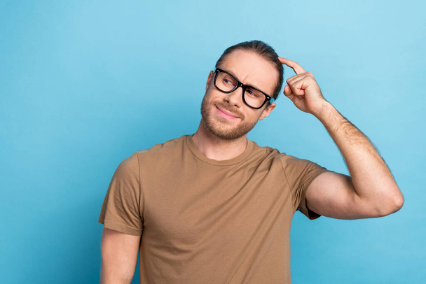 Photo of good mood smart guy with tail hairdo dressed beige t-shirt thoughtfully look empty space isolated on blue color background. - Foto, Bild