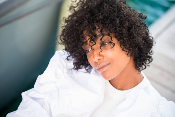 Headshot van zorgeloze pensive afro-Amerikaanse jonge meisje in de buitenlucht. Mooi Afrikaans model denken alleen. Zwart krullend haar. Serene vrouw met witte trui - Foto, afbeelding