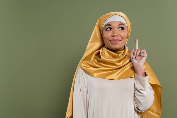 Sonriente mujer multirracial en hiyab teniendo idea aislada en verde  - Foto, Imagen