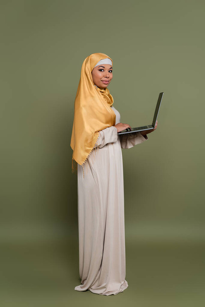 Jeune femme multiraciale dans le hijab en utilisant un ordinateur portable sur fond vert - Photo, image