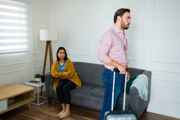 Annoyed upset man with a suitcase moving and leaving his wife after splitting up and having a divorce - Photo, Image