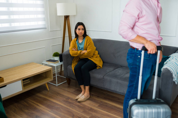 Sad latin woman looking depressed watching her husband leave the marriage and moving with a suitcase - 写真・画像