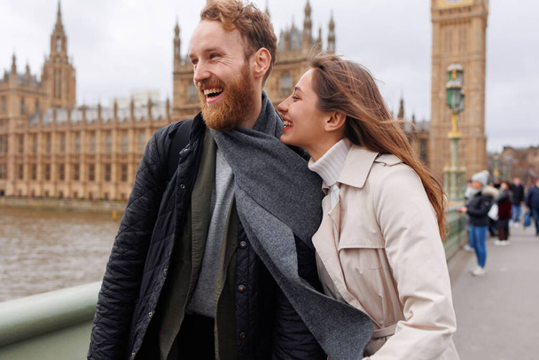Mutlu genç çift, Londra 'nın Big Ben' inin arka planında el ele tutuşarak yürüyor. - Fotoğraf, Görsel