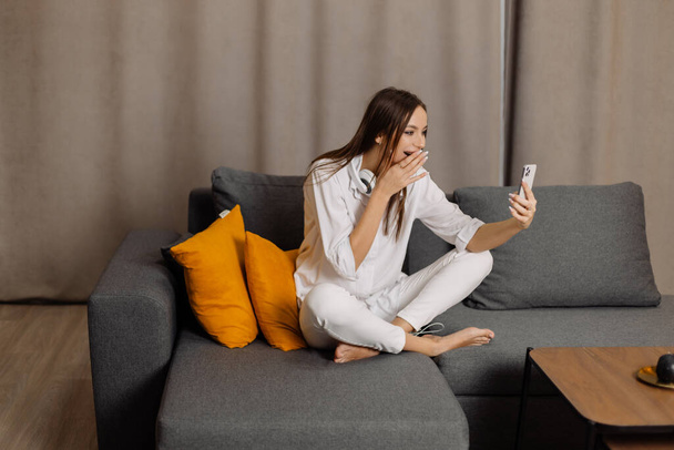 Счастливая и улыбающаяся белая женщина в наушниках использовать мобильный телефон есть веб-камера цифровой онлайн связи дома. - Фото, изображение