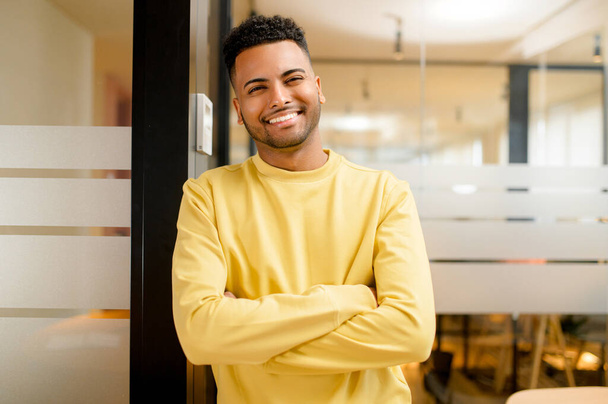 Smiling indian businessman standing in modern open space office and looking at the camera. Young positive male student, proud and successful multiracial small business owner - Valokuva, kuva