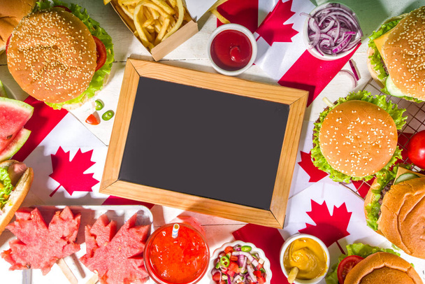 Sada různých kanadské den bbq potravin. piknikový stůl s javorovým listem ve tvaru melounu, vlajky, burgery, hot dogy, hranolky a omáčky, studené nápoje, bílý stůl s červeným dekorem, horní pohled kopírovací prostor - Fotografie, Obrázek
