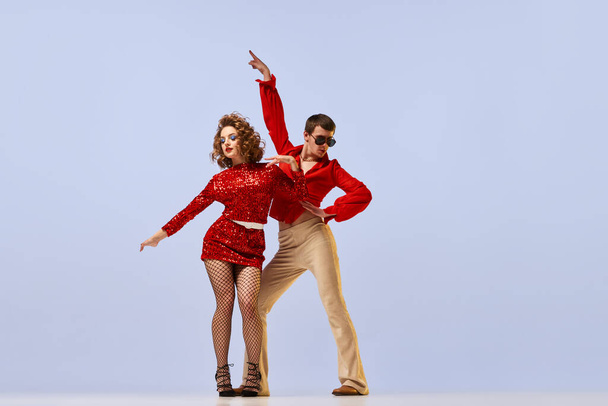 Disco ballroom dances. Young beautiful couple of dancers in bright retro fashion clothes, stage costumes dancing over lilac color background. Concept of music, art, vintage - Foto, Imagen