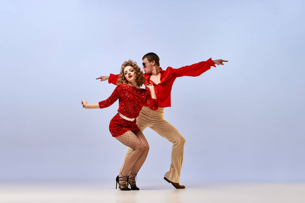 Disco ballroom dances. Young beautiful couple of dancers in bright retro fashion clothes, stage costumes dancing over lilac color background. Concept of music, art, vintage - Foto, Imagem