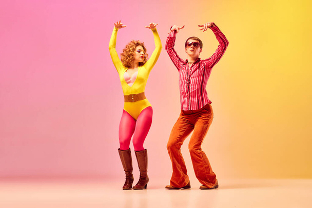 Stylish expressive excited couple of professional dancers in retro style clothes dancing disco dance over pink-yellow background. Concept of 70s, 80s fashion style, music and emotions - Fotoğraf, Görsel