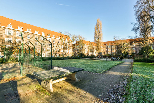 Amszterdam, Hollandia - 2021. április 10.: egy park egy városi terület közepén fákkal és épületekkel mindkét oldalon, van egy pad az embereknek, hogy üljenek - Fotó, kép
