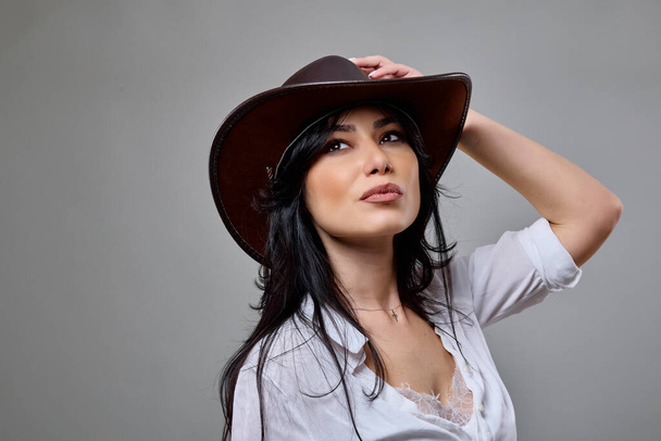 Porträt einer schönen brünetten Frau im lässigen Outfit mit Hut im Studio - Foto, Bild