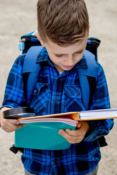 A smart little student with a magnifying glass reads a textbook, explores new things. - Foto, afbeelding