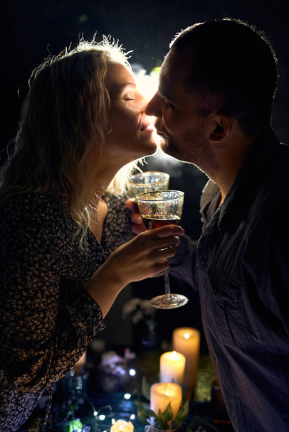 Een romantische close-up van een elegant koppel met wijnglazen, verlicht met sfeervolle achtergrondverlichting en rook, met kaarsen op tafel die een intieme sfeer creëren. - Foto, afbeelding