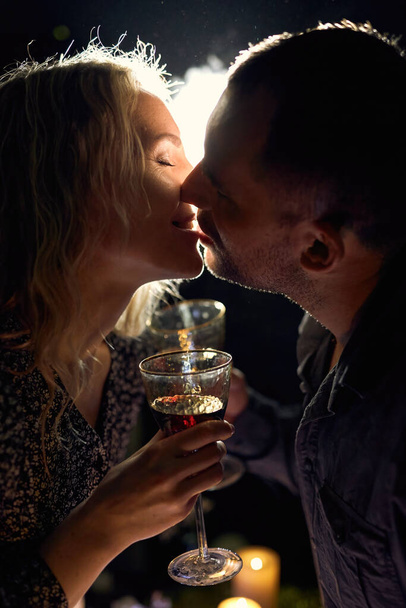 Un romántico primer plano de una elegante pareja sosteniendo copas de vino, iluminadas con luz de fondo malhumorado y humo, con velas sobre la mesa creando un ambiente íntimo. - Foto, imagen