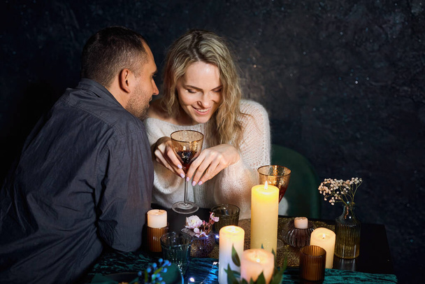 Ein romantisches Paar in einem schummrig beleuchteten Restaurant mit flackernden Kerzen, der Mann flüstert seiner Geliebten süße Kleinigkeiten ins Ohr. - Foto, Bild