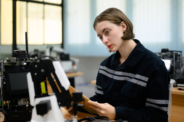 Female technician engineer using laptop checking and operating automatic robotic machine at industrial factory, Worker working with robotic system in factory - Fotó, kép