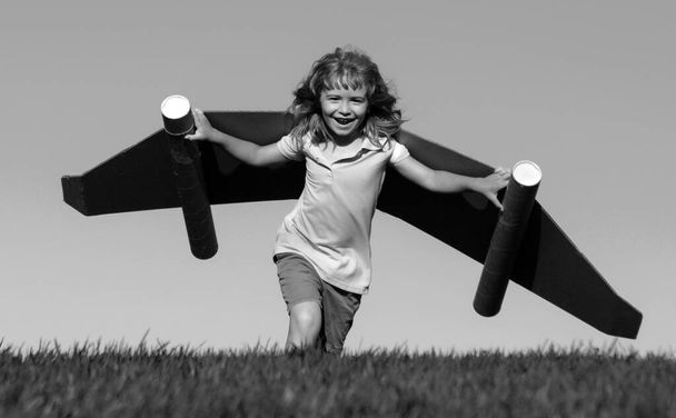 Banner with spring kids portrait. Happy child with paper wings against blue sky. Kid with toy jetpack having fun in spring green field outdoor. Freedom carefree and kids imagination dream concept - Foto, imagen