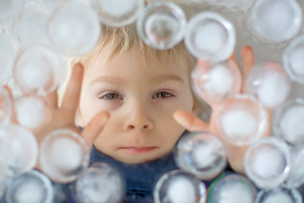 Portrait of blond toddler boy, lying under ice cubes, looking at camera, creative child portrait - Foto, immagini