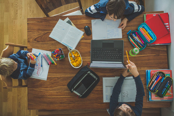 Tres niños, sentados alrededor de la mesa, escribiendo tareas escolares durante la educación en el hogar, mientras que la escuela cerró debido al Coronavirus - Foto, imagen