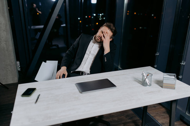 cansado y estresado joven oficinista o empresario trabaja hasta tarde en el escritorio con su computadora portátil - Foto, imagen