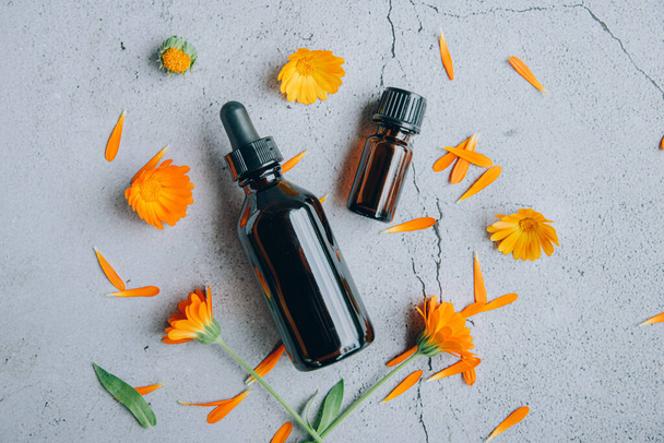 Draufsicht auf Glasflaschen mit ätherischem Calendula-Öl mit frischer Ringelblume orange gelbe Blüten und Blütenblätter über grauem Hintergrund Aromatherapie-Konzept. - Foto, Bild