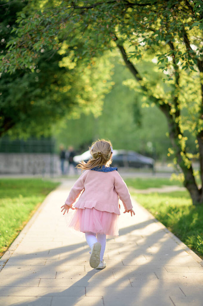 A little girl 3 years old in a summer dress runs away from the camera. The girl is turned back. Summer time. - Fotografie, Obrázek