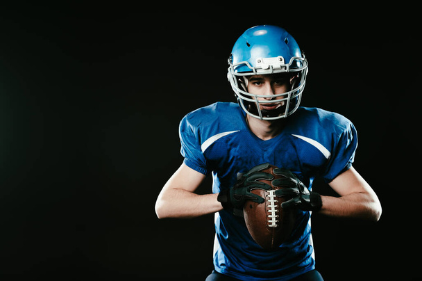 Portrait of a man in a blue uniform for american football on a black background - Фото, изображение