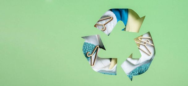 Des vêtements colorés et des mini-affamés sous le symbole de recyclage du papier coupé. Occasion, don de vêtements. Réutilisation, concept de recyclage. - Photo, image