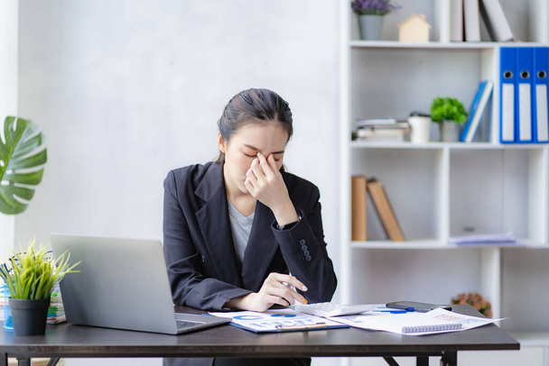 Asian businesswoman holding her head because of headache at work with too much paperwork, financial accounting concept - Foto, Imagem