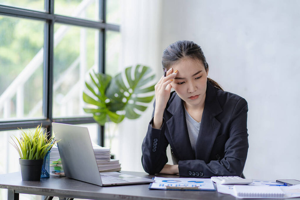 Aziatisch zakenvrouw houden haar hoofd vanwege hoofdpijn op het werk met te veel papierwerk, financiële boekhouding concept - Foto, afbeelding
