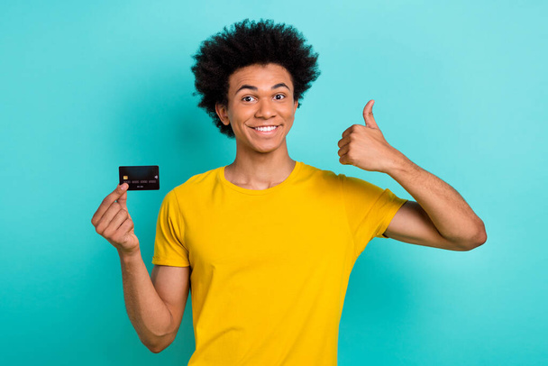Photo of positive guy afro hairstyle dressed yellow t-shirt showing like approval hold card isolated on turquoise color background. - 写真・画像