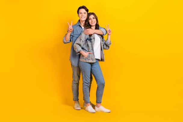 Full length photo of sweet pretty couple wear jeans showing v-signs cuddling isolated yellow color background. - Foto, immagini