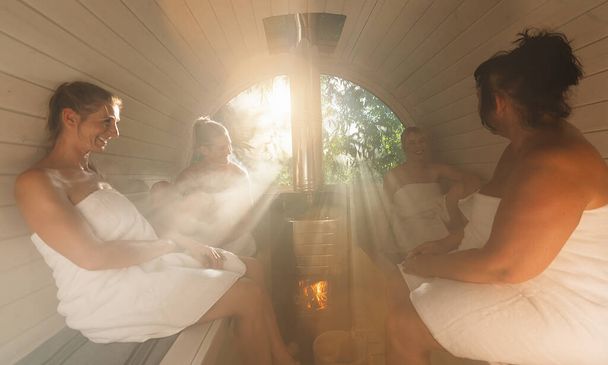 Groupe de personnes assises avec des serviettes dans un sauna en baril en bois chaud au nord. Sont détendus, riant et profiter des vacances tout en se relaxant dans la cabine de sauna finlandaise. - Photo, image