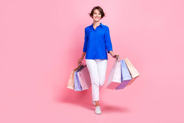 Ganzkörpergröße Fotomodell junge Frau tragen Business-Stil formale Kleidung zu Fuß mit Einkaufszentrum Taschen isoliert pastellrosa Farbe Hintergrund. - Foto, Bild