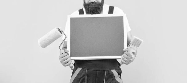 cropped man in work clothes hold paint roller brush and blackboard with copy space on yellow background. - Valokuva, kuva