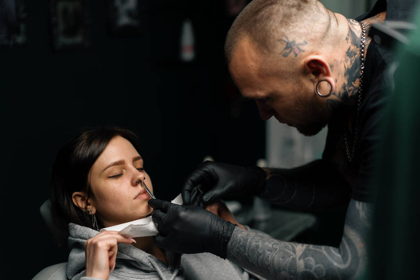 Piercing-Studio - ein Meister sticht einem Mädchen in die Nase - Foto, Bild