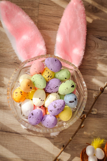 Glass plate with painted colorful eggs and pink Easter bunny ears on a wooden background. Easter religious holiday concept. Vertical photo. High quality photo - Valokuva, kuva