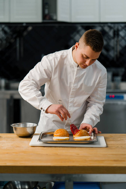 A chef butters burger buns with a brush in professional kitchen gastronomy - Foto, Bild
