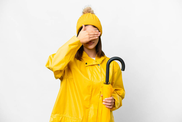 Yağmura dayanıklı paltosu ve şemsiyesi olan genç bir Rus kadın izole edilmiş beyaz arka planda elleriyle gözlerini kapatıyor. Bir şey görmek istemiyorum. - Fotoğraf, Görsel