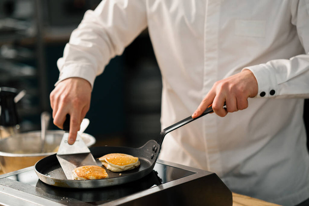 The cook prepares pancakes or pancakes for breakfast in a professional kitchen the pancake is removed from pan - Fotó, kép
