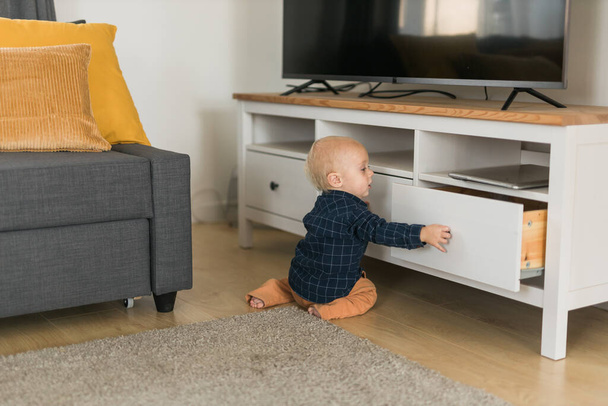 Toddler baby boy open cabinet drawer with his hand. Child explore what is in cabinet. Baby curiosity and child development stages concept - Foto, afbeelding