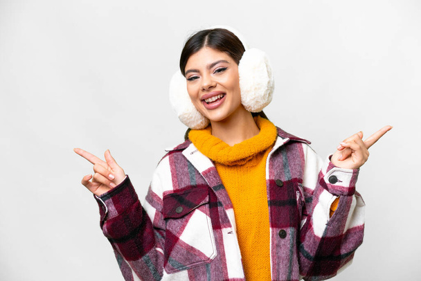 Nuori venäläinen nainen yllään talvi muffinsseja yli eristetty valkoinen tausta osoittaa sormella laterals ja onnellinen - Valokuva, kuva