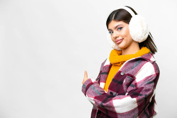 Young Russian woman wearing winter muffs over isolated white background pointing back - Foto, immagini