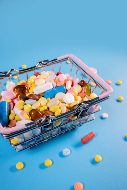 Various capsules, pills and medicines in a shopping cart on a blue background. Health care, treatment. The concept of buying pills and buying medicine. - Photo, image