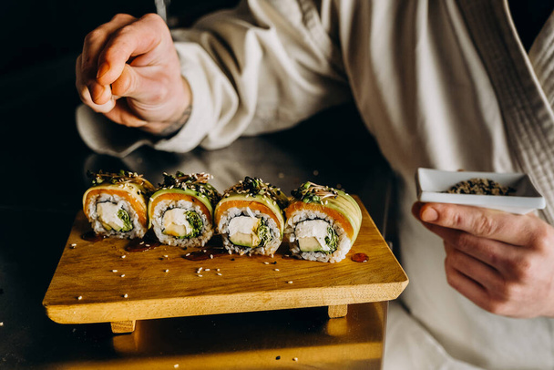 Mistrz sushi robi świeże, apetyczne sushi. Posypać nasiona sezamu na wierzchu bułek. - Zdjęcie, obraz