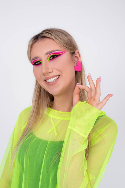 Its okay. Young blonde with bright neon makeup smiles and shows with her fingers that everything is fine in camera. Profession of makeup artist. Modern fashion trends. Creative image. Beauty.  - Foto, imagen