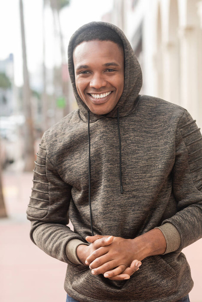 overjoyed african american man in hooded sweatshirt looking at camera while smiling outdoors  - Foto, imagen